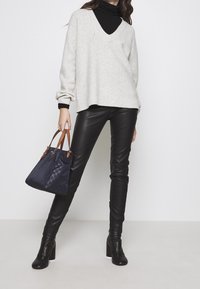 Vaaleanharmaa neulepusero, jossa on V-aukkokohta, musta poolopaita alla, mustat nahkahousut ja sininen käsilaukku ruskeilla kahvoilla.