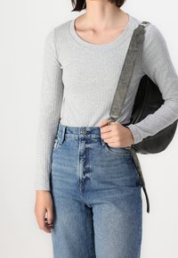 Ljusgrå ribbad långärmad topp i kombination med högmidjade blå denimjeans. En svart axelväska med texturerad rem syns också.