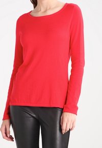 Haut rouge à manches longues avec un col rond, fabriqué en tissu doux, présentant un design ajusté. Associé à un pantalon en cuir noir.