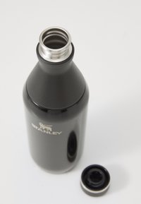 Bouteille d'eau en acier inoxydable noir avec un design effilé, ouverture filetée argentée et un couvercle noir reposant à côté. Logo "STANLEY" visible.