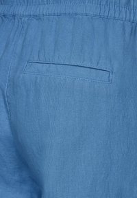 Lichtblauwe linnen stof met een elastische tailleband en een enkele, platte achterzak. De textuur is iets gekreukt en zacht.