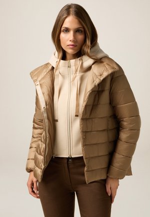 Lichte bruine pufferjack met horizontaal quiltpatroon, voorzien van een afneembare capuchon en gouden hardware. Draagt over een crèmekleurige hoodie.