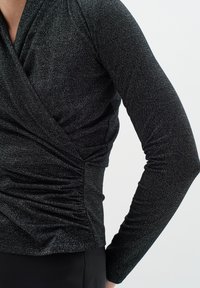 Top nero a maniche lunghe realizzato in tessuto testurizzato con una leggera brillantezza, caratterizzato da un design avvolgente e dettagli arricciati in vita.