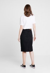 Falda lápiz de mezclilla negra con dobladillo deshilachado y bolsillos traseros, combinada con una camiseta blanca y zapatillas negras.