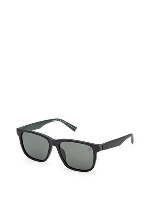 Gafas de sol rectangulares negras con lentes de tono oscuro y un logotipo sutil en la patilla, inclinadas ligeramente hacia la derecha sobre un fondo blanco.