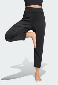 Čierne orezané nohavice z elastickej látky s vysokým pásom a voľným strihom. Hladká textúra bez viditeľných vzorov alebo kovových doplnkov.