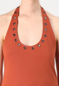 Débardeur couleur rouille avec un décolleté en cœur, présentant des œillets en métal noir le long des bretelles. Tissu doux et extensible.