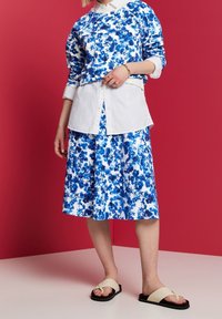 Blommönstrad klänning i blå och vita nyanser, lager med en vit skjorta under. Lätta skor med minimalistisk design.