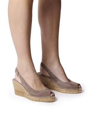 Sandales compensées en daim beige avec un bout ouvert, une sangle arrière et des détails en jute tressé sur le talon compensé. Texture lisse et forme courbée.