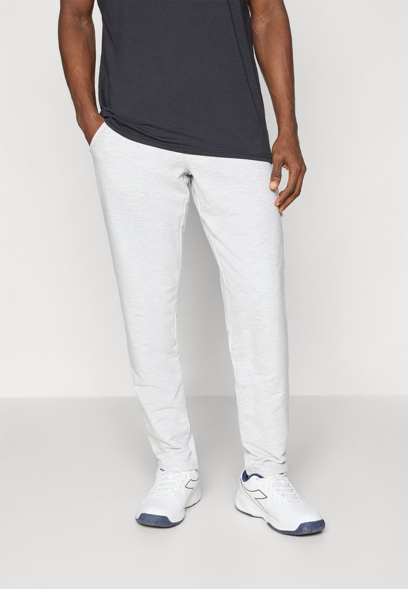 Pantalones de chándal gris claro con un corte ajustado, que presentan una textura suave, cinturilla elástica y bolsillos laterales, combinados con zapatos deportivos blancos.