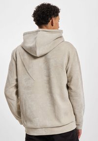 Beige kordfløyelshettegenser med en stor, stoffforet hette og ribbet tekstur. Har en avslappet passform og avrundet kant.