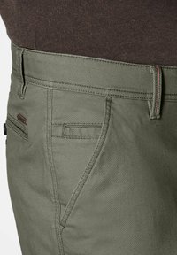 Olivgrüne Hosen aus strukturiertem Stoff, mit einer Vordertasche, dezenten Akzenten und einem kontrastierenden roten Stichdetail.