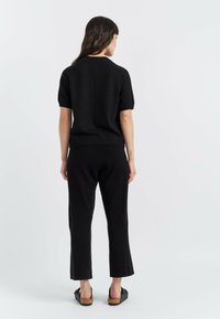 Schwarzes gestricktes T-Shirt mit kurzen Ärmeln, kombiniert mit passgenauen, maßgeschneiderten Hosen, die ein tailliertes Design aufweisen, und flachen schwarzen Slippern.