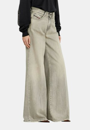 Persona che indossa jeans grigio chiaro a vita alta e gamba larga e una maglia nera a maniche lunghe con logo visibile sulla manica.