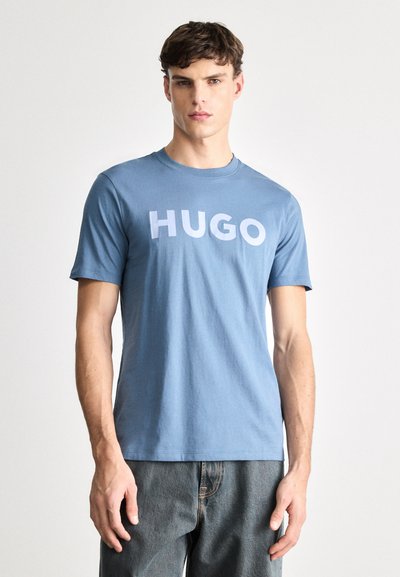 Синя памучна тениска с къси ръкави, на която е изписано името "HUGO" с бледи букви през гърдите. Класически кръгъл деколте.