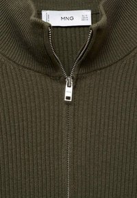Olivno zelena rebrasta zip-up jopica z visokim ovratnikom in kovinskim zadrgo, opremljena z majhnim blagovnim znamčnim oznakom na notranji etiketi.