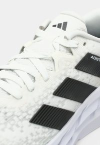 Witte sportshoe met een gestructureerd patroon, zwarte accenten en drie zwarte strepen. Ronde veters en gewatteerde kraagdetails.