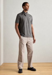 Grå kortärmad T-shirt med en svart scarf, matchad med ljusbeige byxor och svarta skor. Enkelt design med minimala detaljer.