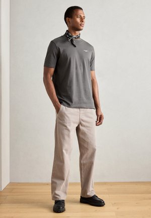 Gray short-sleeve T-shirt with a black scarf, paired with light beige pants and black shoes. Simple design with minimal details.