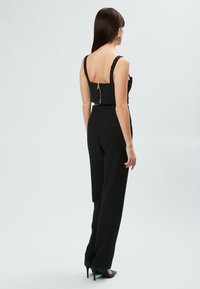 Conjunto de dos piezas negro que incluye una parte superior corta con cremallera en la parte posterior y pantalones de tiro alto. El material tiene una textura suave.