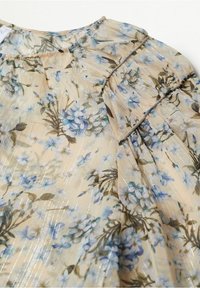 Floral blouse featuring a lightweight, sheer beige fabric with blue and green floral prints, accented by subtle metallic threads and ruffled details.