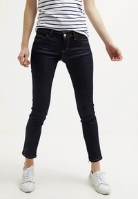 Vaqueros ajustados de denim oscuro con cintura de altura media, que cuentan con cinco bolsillos, costuras en contraste y cremalleras en los tobillos.