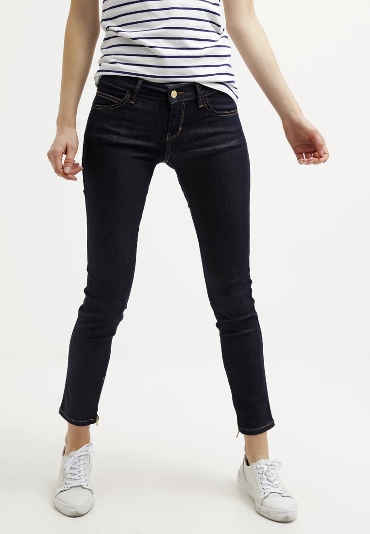 Vaqueros ajustados de denim oscuro con cintura de altura media, que cuentan con cinco bolsillos, costuras en contraste y cremalleras en los tobillos.