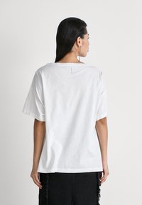 Hvit oversized bomulls T-skjorte med rund hals, korte ermer og en liten løkke detalj bak. Kombinert med sorte teksturerte shorts.