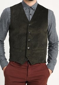 Gilet in suede verde oliva scuro con scollo a V, cinque bottoni e due tasche frontali, indossato su una camicia grigia. Design strutturato e aderente.