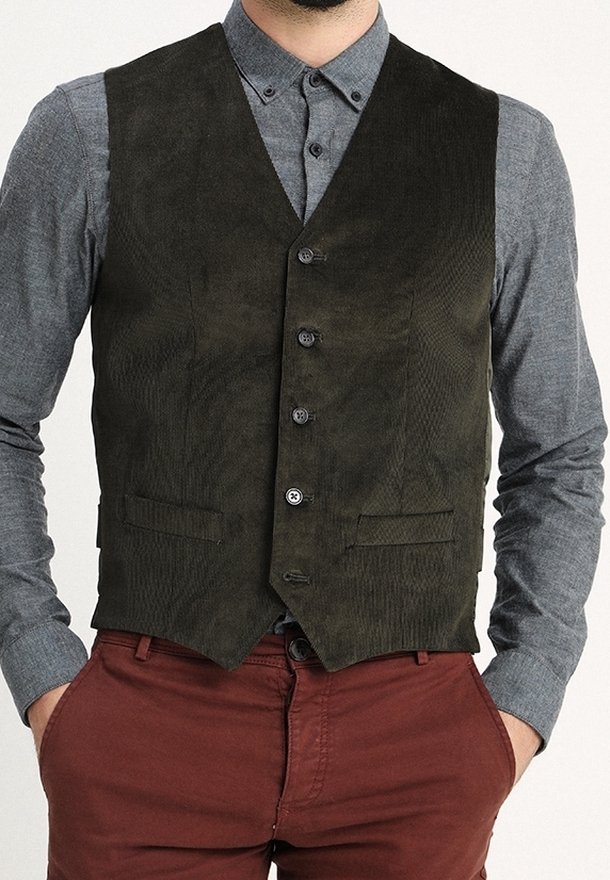 Gilet in suede verde oliva scuro con scollo a V, cinque bottoni e due tasche frontali, indossato su una camicia grigia. Design strutturato e aderente.