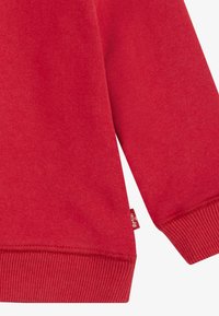 Manga y dobladillo inferior de sudadera roja con puños acanalados y una pequeña etiqueta de marca en la costura lateral.