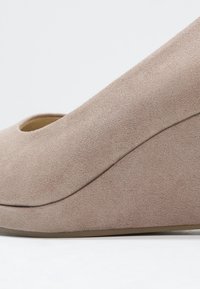 Chaussure compensée en daim beige avec bout arrondi, semelle plateforme cachée et tige à texture lisse.