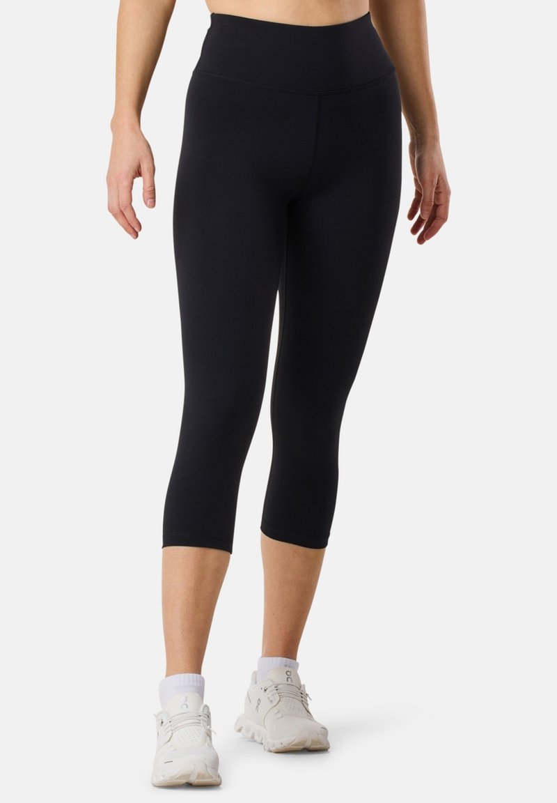 Leggings atletici neri con vita alta e lunghezza cropped, realizzati in tessuto morbido, abbinati a sneakers bianche e calzini di lunghezza normale.