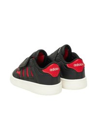 Scarpe per bambini nere e rosse con tomaia sintetica, cinturino in velcro, suola in gomma bianca e tre strisce rosse sul lato.