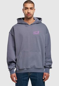 Felpa con cappuccio grigia realizzata in materiale morbido, dotata di una tasca frontale e di un logo grafico rosa sul lato sinistro del petto. Vestibilità ampia.