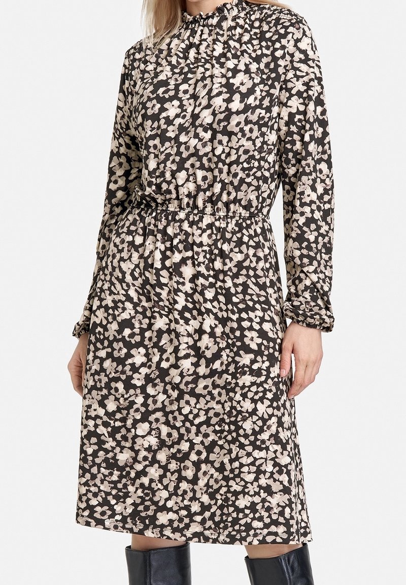Robe à manches longues avec un motif floral foncé comprenant des fleurs blanches et beiges, encolure froncée et taille élastique. Texture de tissu lisse.