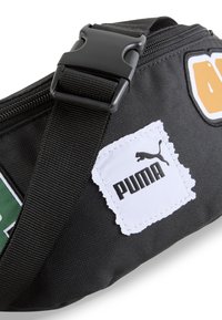 Fekete szövet tasak állítható pánttal, műanyag csat, hímzett foltok és egy fehér címke fekete Puma logóval.