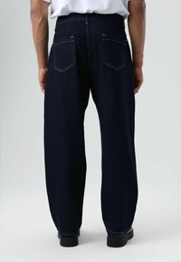 Donkerblauwe spijkerbroek met een ontspannen pasvorm, voorzien van zichtbare naden, twee achterzakken en een rechte pijp.