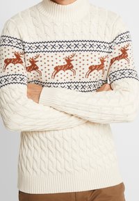 Krämfärgad kabelstickad tröja med ett renmönster i bränd orange med mörkblå accenter, rullad krage och ribbade ärmslut och nederkant.