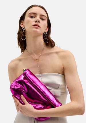 Clutch metálico fucsia con una textura suave y brillante y un diseño de doblez, sostenido contra un top sin tirantes de color claro.