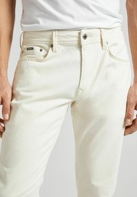 Jean en denim blanc avec une coupe slim, dotés de cinq poches, de coutures discrètes et d'un accent en métal sur la poche avant.