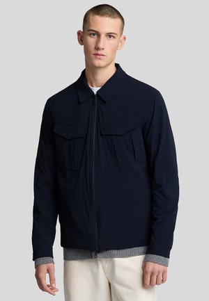 Veste marine avec une fermeture éclair sur le devant, un col plat, deux poches sur la poitrine et un pull gris côtelé en dessous. Tissu lisse avec une coupe moderne.