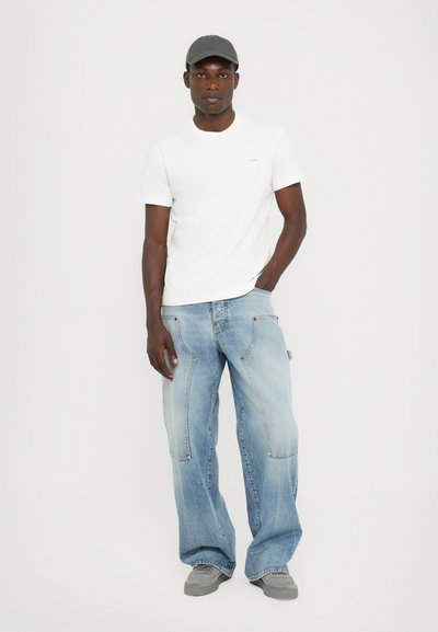 Vit t-shirt med kort ärm, ljusbl�å baggy jeans med fickor, grå keps och grå skor. Enkel design, avslappnad passform och ljusa färger.