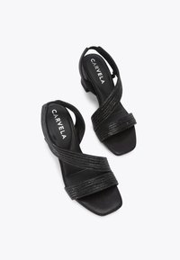 Zwarte slingback sandalen met textuur, gekruiste banden, vierkante neus en een lage blokhak, met een smooth afwerking en minimale hardware.