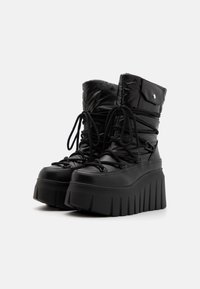 Botas de plataforma negras con una textura esponjosa, que presentan un cierre de cordones en la parte delantera, una suela alta y estriada, y un detalle de puño doblado en la parte superior.