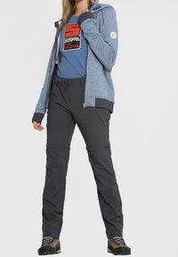 Blå zip-up hoodie, grå byxor med fickor och robusta bruna utomhusskor. Huva med kontrasterande muddar och logotypdetalj på tröjan.