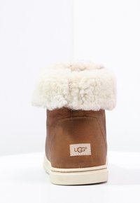 Botte en daim marron avec un col en shearling crème duveteux, dotée d'une étiquette de marque et d'une semelle en caoutchouc blanche. Surface texturée avec un design court.