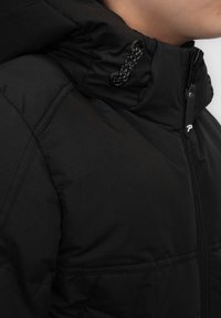 Giacca imbottita nera con colletto alto, dotata di chiusura con zip, tessuto texture e cappuccio con cordoncino per una vestibilità regolabile.