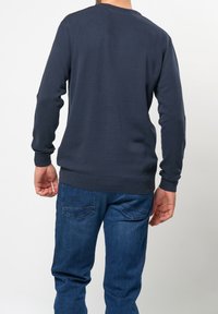 Marinblå sweatshirt med långa ärmar, ribbade ärmslut och nederkant. Mjuk, texturerad tyg; buren med blå jeans, vilket visar bakvyn.