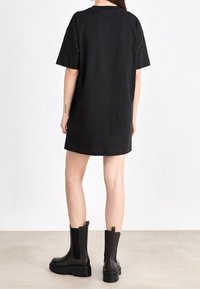 Czarna bawełniana sukienka t-shirtowa z krótkimi rękawami, luźnym krojem i okrągłym dekoltem. W komplecie z czarnymi botkami do kostki na grubej podeszwie.